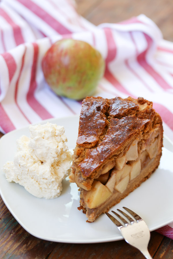 dutch apple pie with whipped cream on a white plate with a red and white striped dishtowel in the background