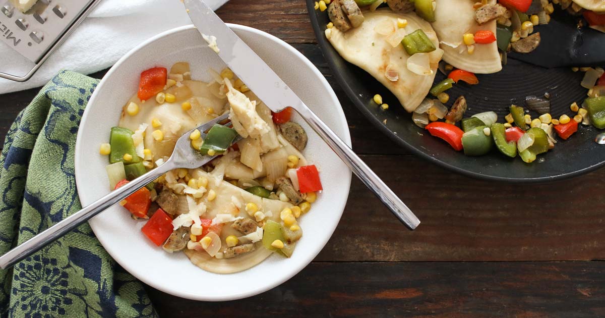 pierogies with onions, peppers, and sausage in a white bowl on a wooden background