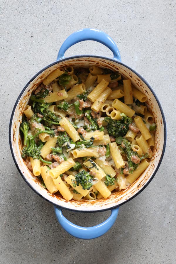  baked pasta with sausage and broccolini in a blue dutch oven on a grey background