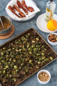 roasted brussels sprouts on a sheet pan surrounded by bowls of figs and hazelnuts and a plate of cooked bacon