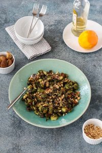 roasted brussels sprouts with bacon and figs on a teal plate with small bowls of figs and hazelnuts