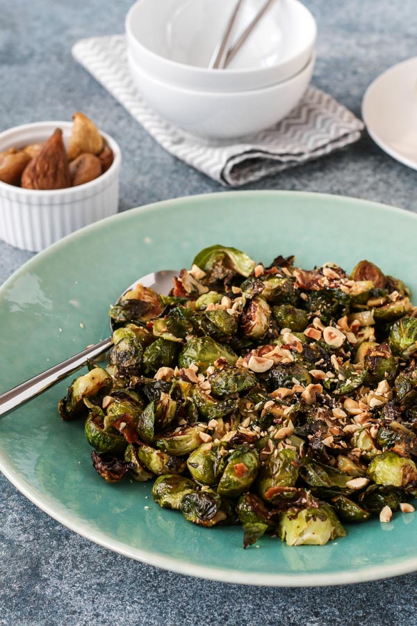 roasted brussels sprouts with bacon and figs on a teal plate with small white bowls in the background