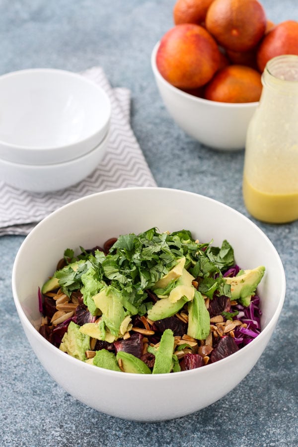 chicken, avocado, and orange salad in a white bowl, topped with avocado and cilantro, with a bowl of oranges in the background