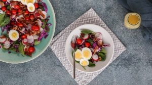 spinach salad with bacon and hard boiled eggs served in a white shallow bowl