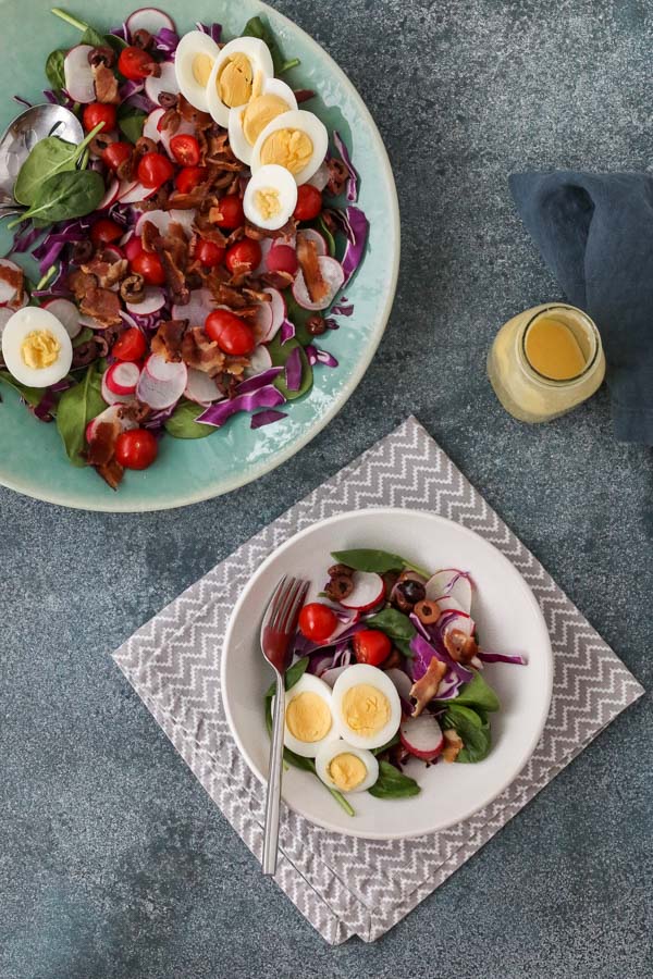 spinach salad with bacon and hard boiled eggs served in a white shallow bowl