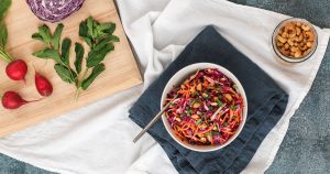 crunchy asian slaw in a white bow with cabbage, radishes, and mint on a cutting board