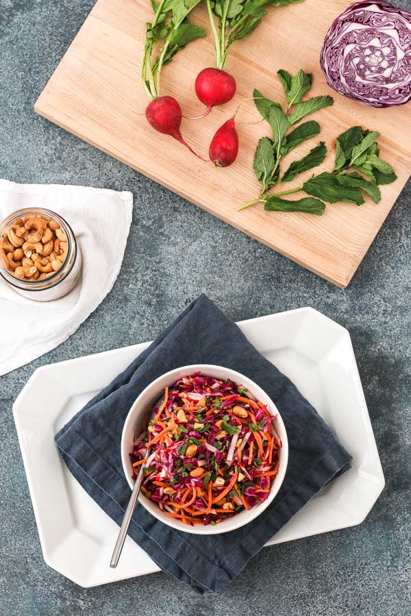 crunchy asian slaw in a white bow with cabbage, radishes, and mint on a cutting board