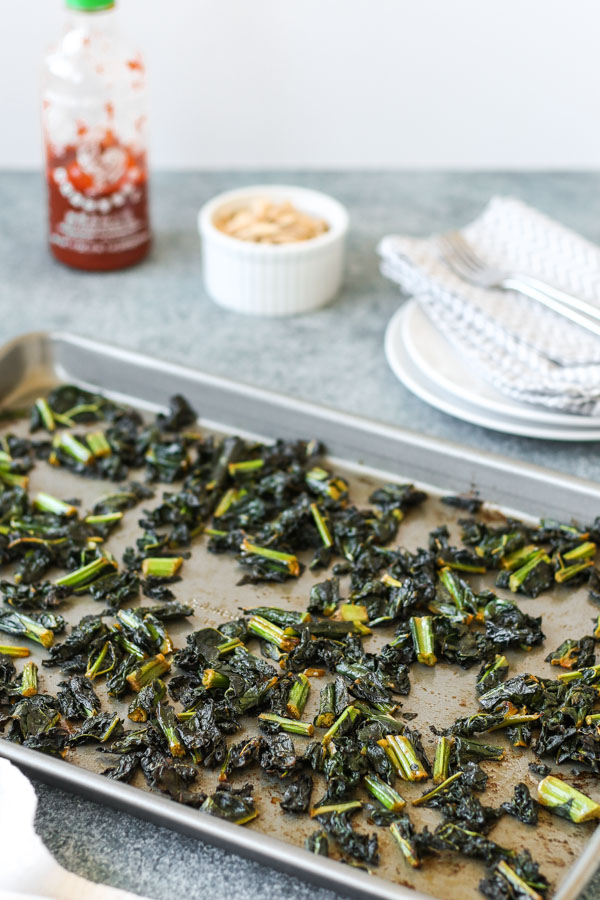 spicy baked kale with almonds on white plates, with a bowl of almonds and a sheet pan in the background