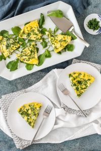 arugula, goat cheese, and chive frittata on a white plate and serving platter