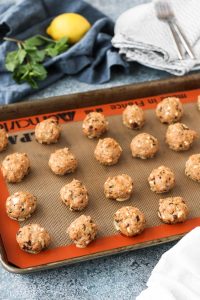 greek turkey meatballs on a rimmed baking sheet with lemon and mint garnishes