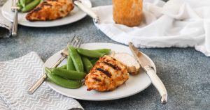 grilled chicken with spicy peanut sauce on white plates served with sugar snap peas