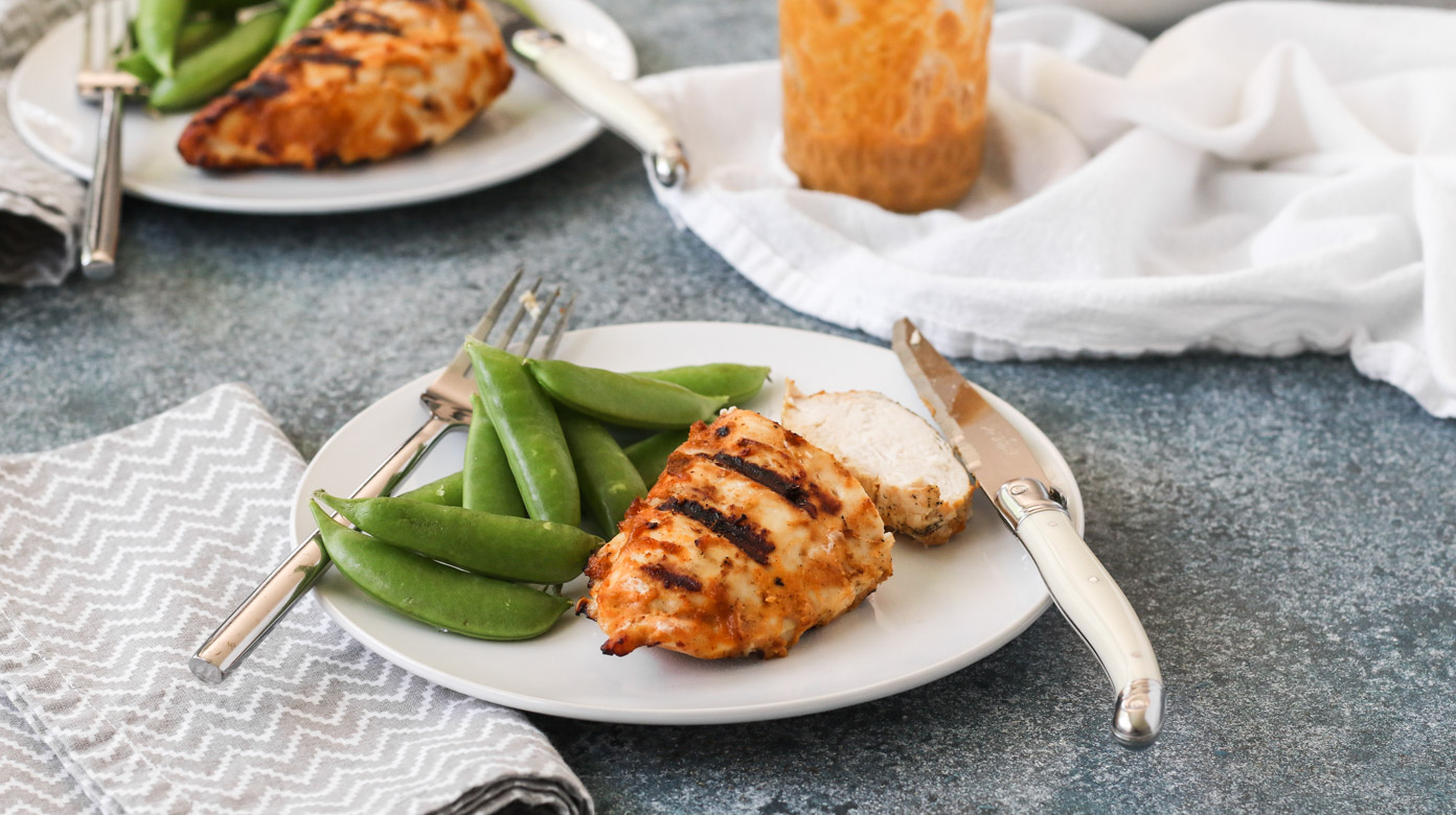 grilled chicken with spicy peanut sauce on white plates served with sugar snap peas