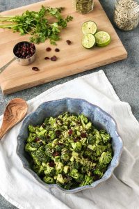 spicy miso tahini broccoli salad with dried cranberries, cilantro, limes, sunflower seeds, and pepitas on a wooden cutting board