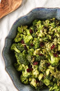 spicy miso tahini broccoli salad with dried cramberries in a blue ceramic bowl on a white background