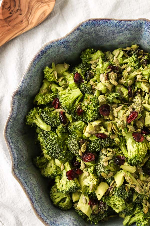 spicy miso tahini broccoli salad with dried cranberries in a blue ceramic bowl on a white background