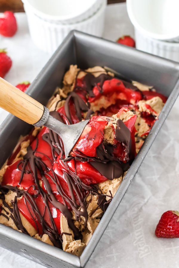 homemade hazelnut ice cream with strawberry and chocolate swirls being scooped out of a metal loaf pan.