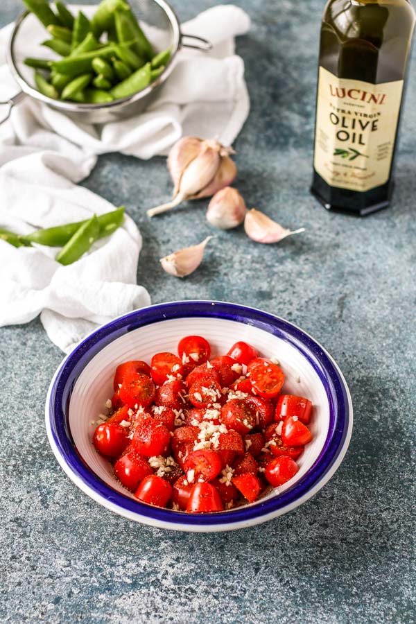 cherry tomatoes marinating in a bowl with garlic, salt, pepper, and olive oil