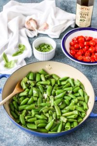 sugar snap peas in a skillet with a bowl of marinated cherry tomatoes